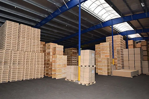 Inside the storage hall: stacks of pallets and crates under the blue steel structure.