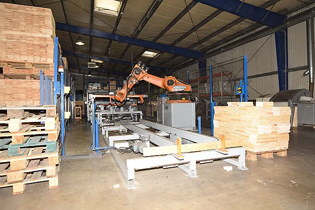 D'Palettemaschinn an der Hal, mat Roboterarm a Holz um Zoulaf.